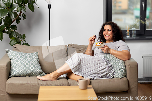 Image of smiling young woman eating cake at home