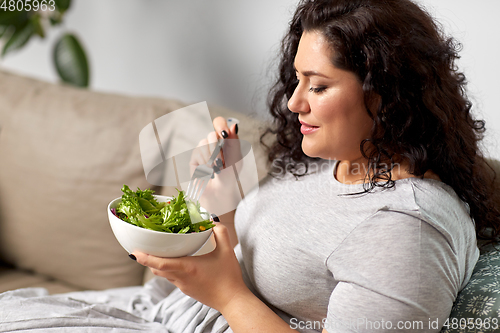 Image of smiling young woman eating vegetable salad at home