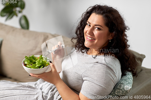Image of smiling young woman eating vegetable salad at home