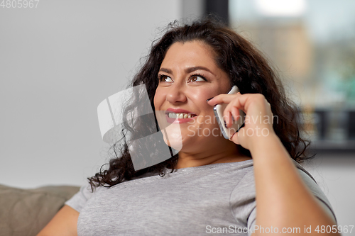 Image of happy young woman calling on smartphone at home