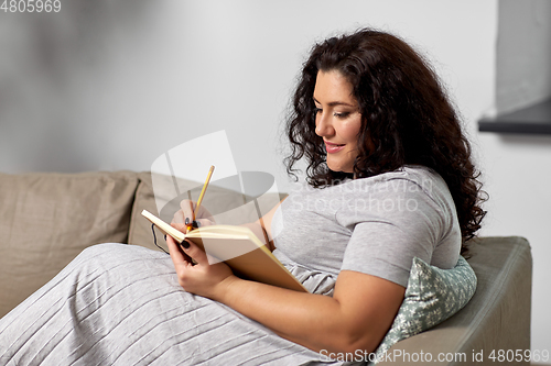 Image of happy young woman with diary on sofa at home
