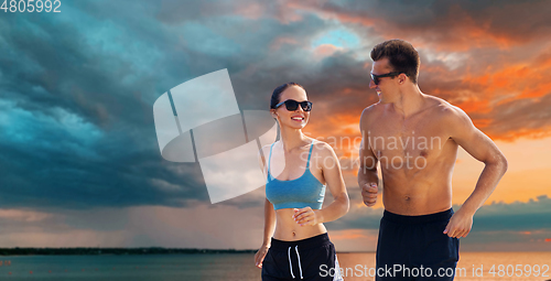 Image of couple in sports clothes running along on beach