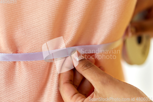 Image of fashion designer's hand attaching ribbon to cloth