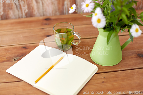 Image of herbal tea, notebook and flowers in jug on table