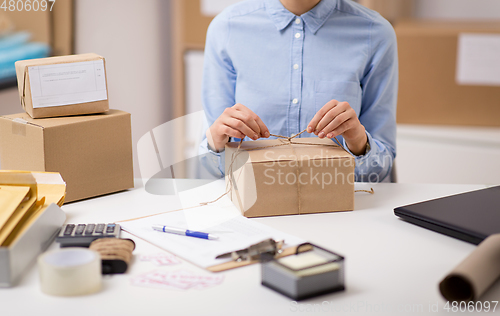 Image of woman packing parcel and tying rope at post office