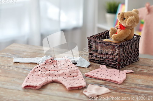 Image of baby clothes and teddy bear toy in basket at home