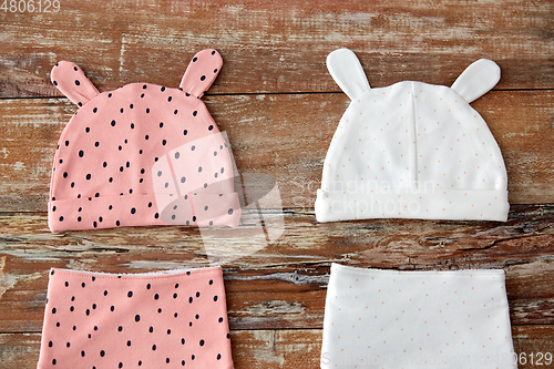 Image of baby hats with ears and bibs on wooden table