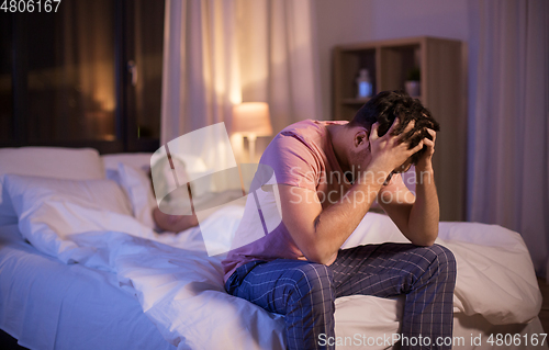 Image of sad man with insomnia sitting on bed at night