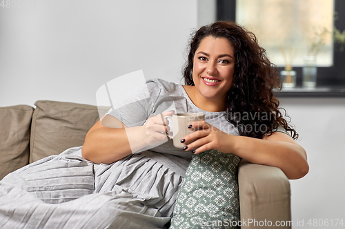 Image of happy woman drinking coffee or tea on sofa at home