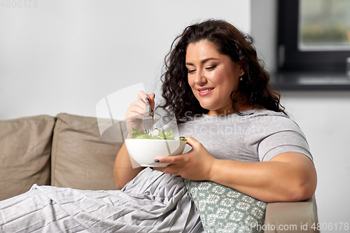 Image of smiling young woman eating vegetable salad at home