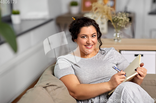 Image of happy young woman with diary on sofa at home