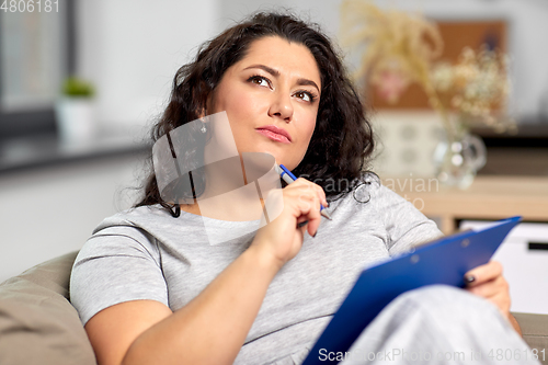 Image of woman with clipboard and pen thinking at home