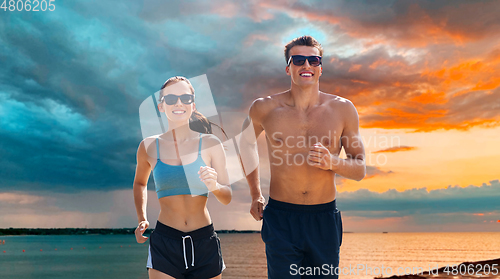 Image of couple in sports clothes running along on beach