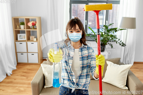 Image of asian woman in protective mask cleaning home