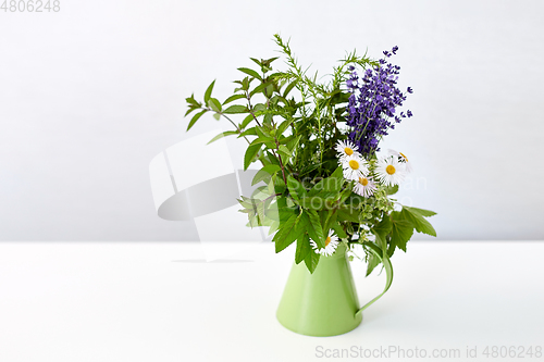 Image of bunch of herbs and flowers in green jug on table