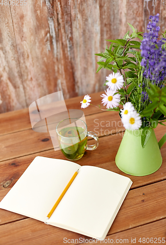 Image of herbal tea, notebook and flowers in jug on table