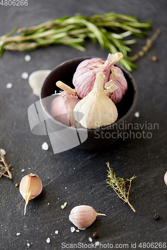 Image of garlic in bowl and rosemary on stone surface