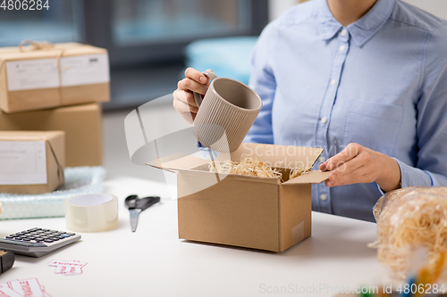 Image of woman packing mug to parcel box at post office