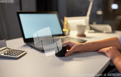 Image of hand using smart speaker at night office