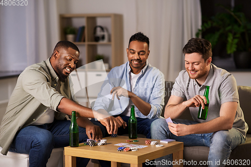 Image of happy male friends playing cards at home at night