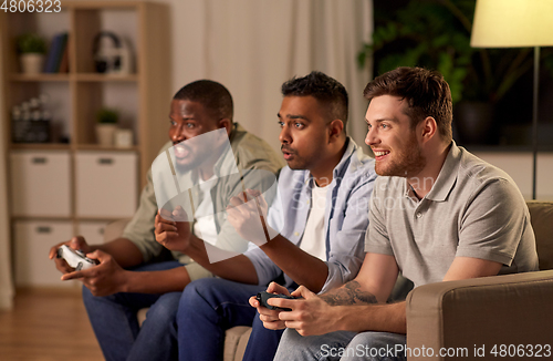 Image of happy friends playing video games at home at night