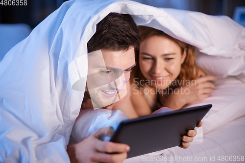 Image of happy couple using tablet pc in bed at night