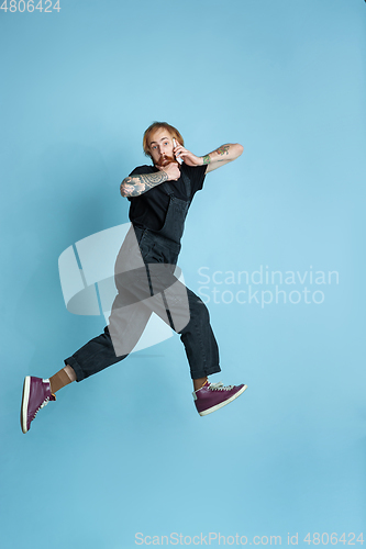 Image of Portrait of young caucasian man looks happy, jumping on blue background