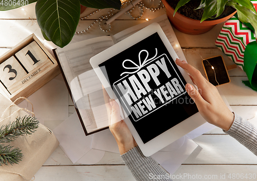 Image of Female hands holding tablet with wishes of happy New Year and Merry Christmas