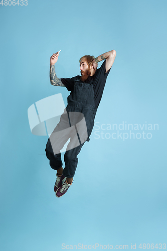 Image of Portrait of young caucasian man looks happy, jumping on blue background