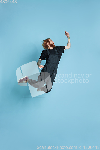 Image of Portrait of young caucasian man looks happy, jumping on blue background