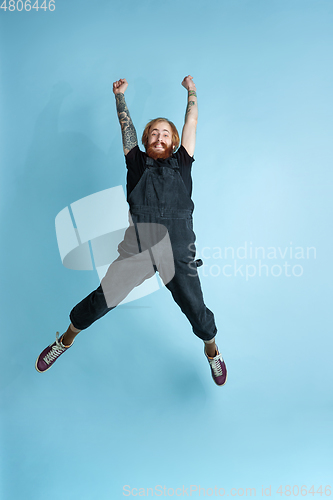 Image of Portrait of young caucasian man looks happy, jumping on blue background