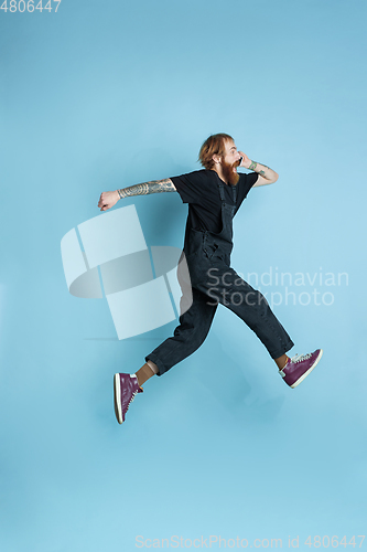 Image of Portrait of young caucasian man looks happy, jumping on blue background