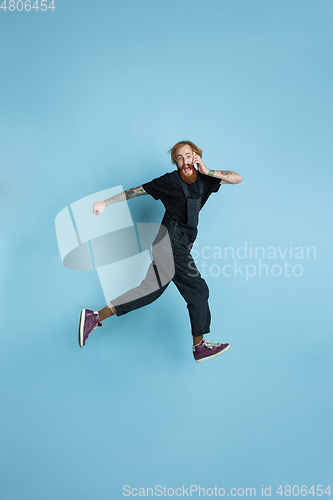 Image of Portrait of young caucasian man looks happy, jumping on blue background