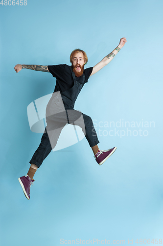Image of Portrait of young caucasian man looks happy, jumping on blue background