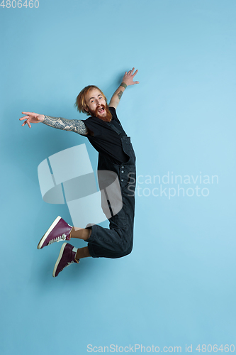 Image of Portrait of young caucasian man looks happy, jumping on blue background