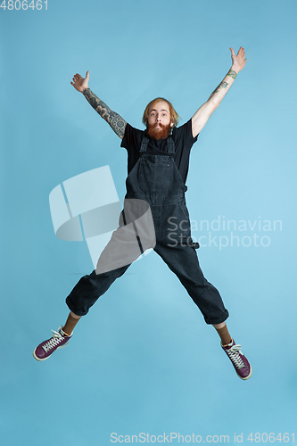 Image of Portrait of young caucasian man looks happy, jumping on blue background