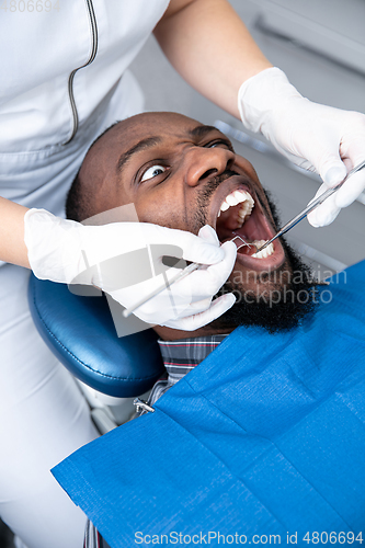 Image of Young african-american man visiting dentist\'s office, looks scared