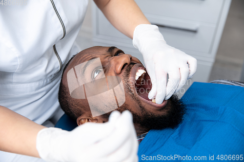 Image of Young african-american man visiting dentist\'s office, looks scared