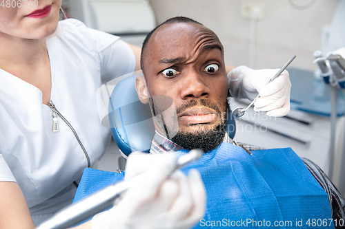 Image of Young african-american man visiting dentist\'s office, looks scared