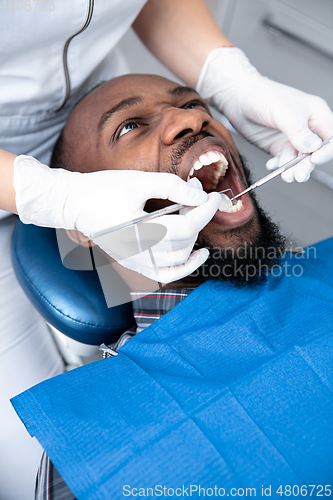 Image of Young african-american man visiting dentist\'s office, looks scared