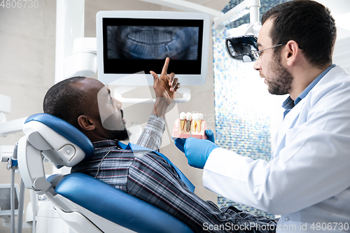 Image of Young african-american man visiting dentist\'s office, using technologies