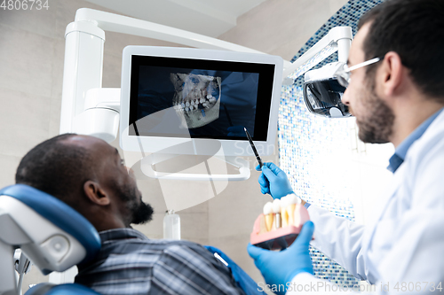 Image of Young african-american man visiting dentist\'s office, using technologies