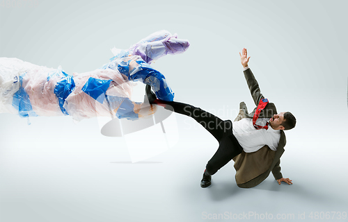 Image of Young caucasian man avoiding big plastic hand on white studio background