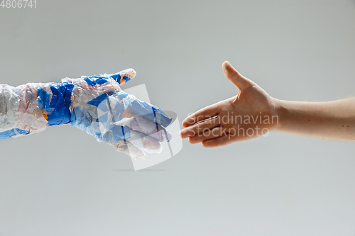 Image of Big plastic hand made of garbage shaking another hand isolated on white studio background