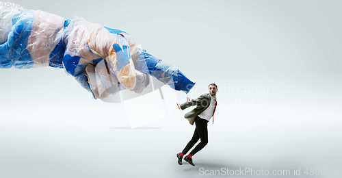 Image of Young caucasian man avoiding big plastic hand on white studio background