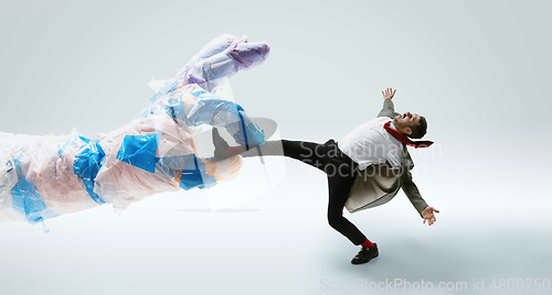 Image of Young caucasian man avoiding big plastic hand on white studio background