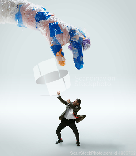 Image of Young caucasian man avoiding big plastic hand on white studio background