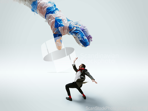 Image of Young caucasian man avoiding big plastic hand on white studio background