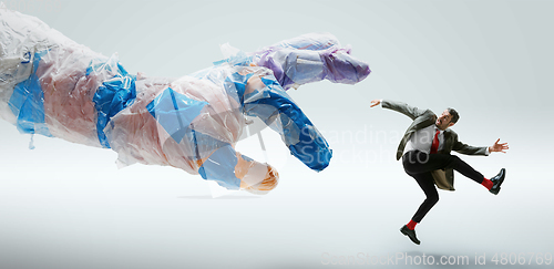 Image of Young caucasian man avoiding big plastic hand on white studio background