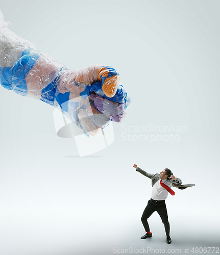 Image of Young caucasian man avoiding big plastic hand on white studio background